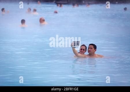 Un couple prend un selfie à la piscine thermale de Blue Lagoon près de Reykjavik en Islande avec de la vapeur qui s'en lève par une journée froide en hiver Banque D'Images
