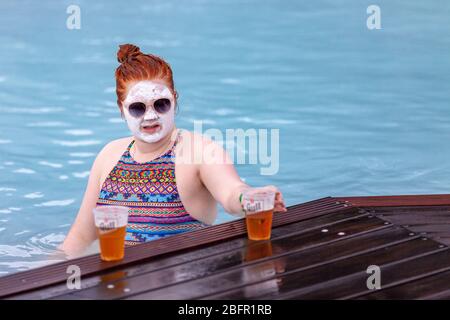 Une femme portant un masque facial de boue boit de la bière à la piscine thermale de Blue Lagoon près de Reykjavik en Islande, par temps froid en hiver Banque D'Images