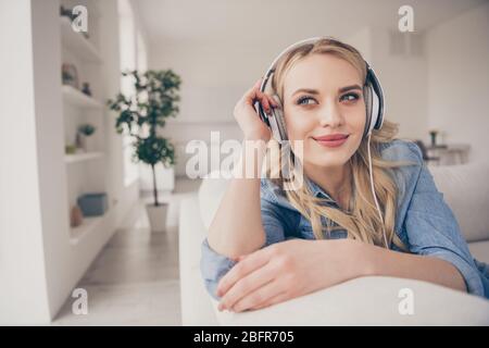 Photo de la charmante dame blonde domestique passer dehors asseyez-vous confortable canapé rester à la maison écoutez les écouteurs cool musique jeunesse rêveur regarder fenêtre Banque D'Images