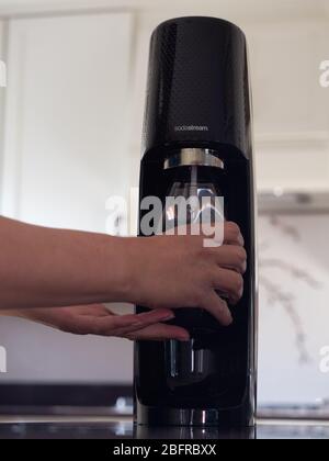 Femme non caucasienne utilisant la Sodastream pour carbonate dans une bouteille en plastique réutilisable dans une cuisine moderne avec des armoires blanches en arrière-plan Banque D'Images