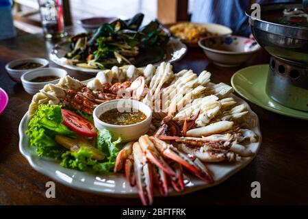 Viande de crabe de natation bleu à la vapeur avec des griffes, des légumes et une sauce de style thaïlandais dans un plat blanc sur une table en bois. Banque D'Images