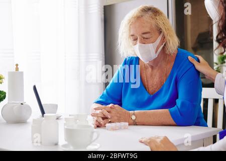 Médecin rassurant la triste femme âgée dans le masque médical après avoir dit son diagnostic Banque D'Images