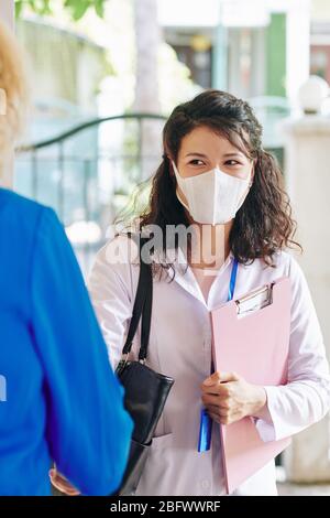 Jeune médecin joyeux en labouret et masque médical en visite chez le patient Banque D'Images