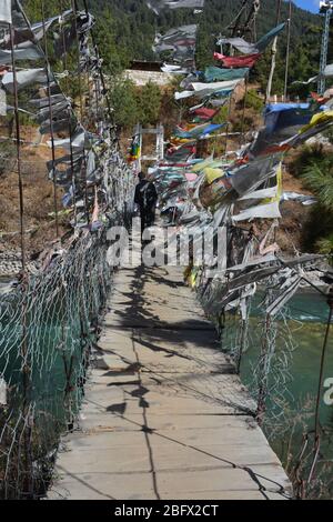 Les drapeaux de prière flottent alors qu'une personne locale marche sur un pont suspendu au-dessus de la rivière Bumthang, au Bhoutan. Banque D'Images