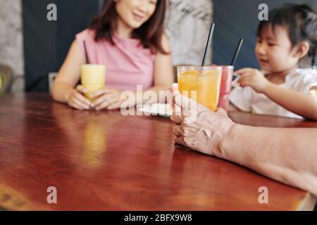 Main de la femme senior buvant un cocktail de fruits lors de la célébration de son anniversaire de petite-fille dans le café Banque D'Images