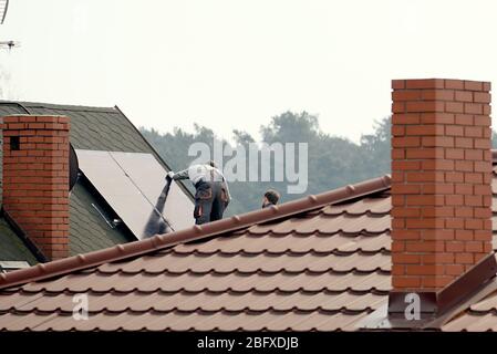 les travailleurs installent des panneaux solaires sur le toit de la maison Banque D'Images