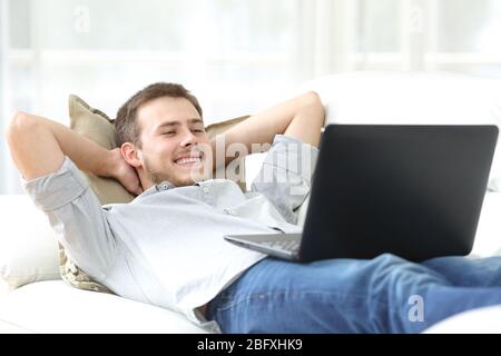 Heureux homme regardant le film en streaming en ligne sur un ordinateur portable allongé sur un canapé à la maison Banque D'Images