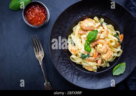 Les pâtes italiennes Les pâtes dans une sauce crémeuse aux crevettes sur une plaque noire, vue du dessus Banque D'Images