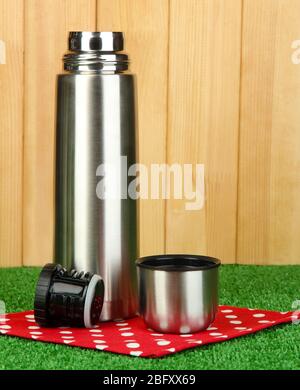 thermos métalliques sur l'herbe sur fond en bois Banque D'Images