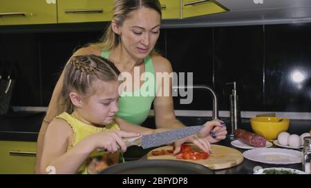 Mère enseignant fille intelligente fille apprendre à cuisiner. Malter les enfants pour faire cuire une omelette au plat napolitain à partir de la saucisse de salame affumicato. Banque D'Images