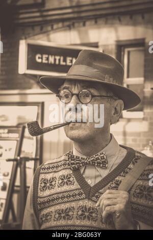 Sépia vintage à l'ancienne près de l'homme isolé avec pipe & trilby chapeau gare ancienne, chemin de fer Severn Valley Railway 1940 guerre été événement Royaume-Uni. Banque D'Images