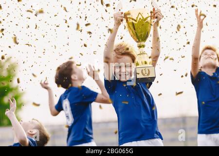 L'équipe sportive célèbre le succès. Heureux garçons montant trophée d'or sur la célébration. Les enfants qui remportant un tournoi de football sportif. Interscolaire ainsi Banque D'Images