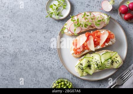 Trois sandwichs avec légumes frais, radis, tomates, concombres et microgreens sur fond gris. Vue de dessus. Espace de copie. Banque D'Images