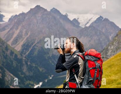 Photographe homme avec de gros sac à dos et appareil photo en photo des montagnes. Style de voyage d'aventure en plein air vacances active concept Banque D'Images