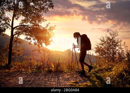 L'homme avec des dreadlocks et son sac à dos en silhouette de la randonnée dans les montagnes en fond de ciel orange au coucher du soleil Banque D'Images