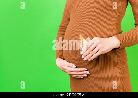 Image rognée d'un paquet de cigarettes sur fond vert. Mauvaise habit d'une femme enceinte. Mère négligente. Banque D'Images