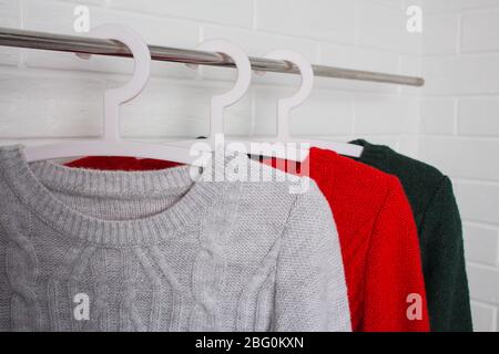 Les vêtements pendent sur les cintres. Sweaters en rouge, vert et couleur mélange. Mode et style, vitrine, magasin, concept. Mur de briques blanches, confort et nettoyage Banque D'Images