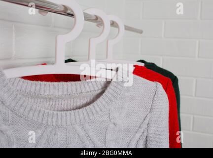 Les vêtements pendent sur les cintres. Sweaters en rouge, vert et couleur mélange. Mode et style, vitrine, magasin, concept. Mur de briques blanches, confort et nettoyage Banque D'Images
