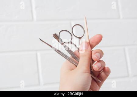 Tenez les outils de manucure dans la main. Soin des ongles, procédure, salon de manucure. Brucelles, coupe-fils, poussoir, bâton orange pour arbres, ciseaux, lime à ongles. Pédicure, Banque D'Images