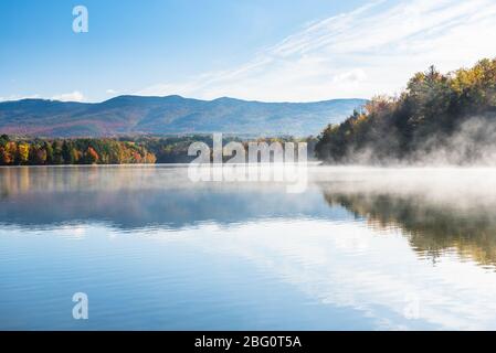 Majestueux lac de montagne foggy avec des rives boisées en automne. Des couleurs d'automne époustouflantes. Banque D'Images