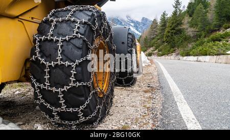 Chargeur frontal pour l'élimination de la neige avec chaînes à neige métalliques sur roues. Déneigement dans les montagnes Banque D'Images