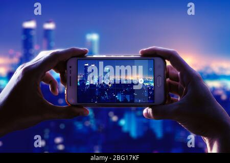 Appareil photo d'un smartphone. Voir à travers l'écran au moment où une jeune femme prend une photo d'une ville la nuit. Paysage urbain. Banque D'Images