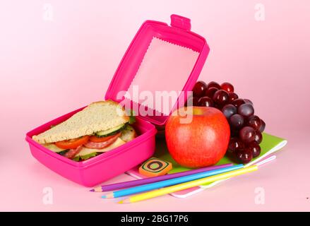 Boîte à déjeuner avec sandwich, fruits et articles de papeterie sur fond rose Banque D'Images