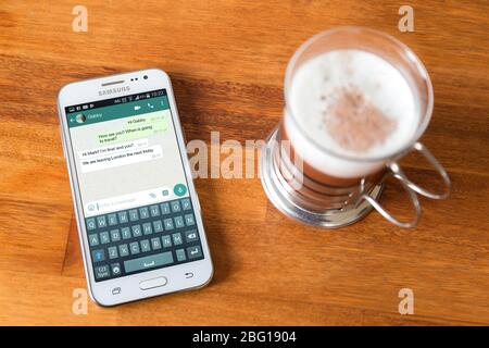 Téléphone portable sur une table en bois près d'une tasse de café. Une discussion de l'application whatsapp à l'écran. Banque D'Images