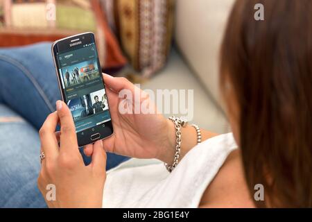 Jeune femme solitaire reposant dans un fauteuil et tenant le téléphone cellulaire avec Amazon Prime web à l'écran. ROSARIO, ARGENTINE - 28 OCTOBRE 2017 Banque D'Images