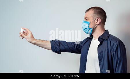 Bouteille de désinfectant de maintien de l'homme dans le masque sur fond gris, Panorama Banque D'Images