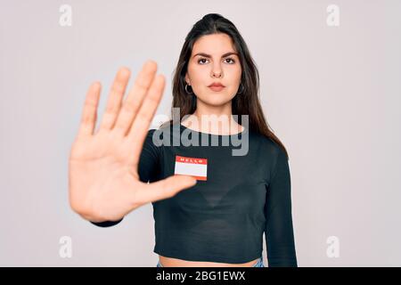 Jeune fille belle portant Bonjour mon nom est autocollant sur fond isolé avec main ouverte faisant signe d'arrêt avec l'expression sérieuse et confiante, d Banque D'Images