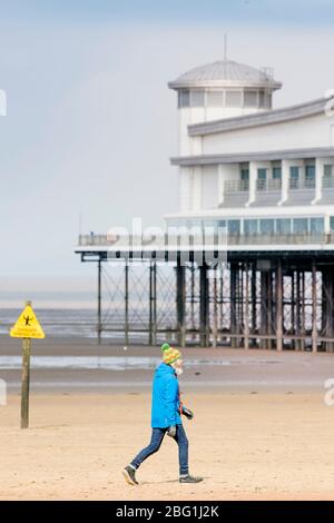Un homme prenant son exercice autorisé quotidien passe devant le Grand Pier de Weston-super-Mare pendant le verrouillage de Coronavirus, au Royaume-Uni Banque D'Images