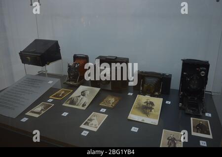 Une collection d'anciens appareils photo pliants et de photographies vintage en noir et blanc exposées dans une vitrine de musée en verre. Banque D'Images