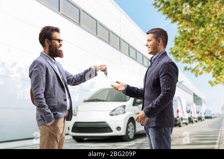 Homme barbu donnant des clés de voiture à un client à l'extérieur d'un bâtiment de service de voiture Banque D'Images