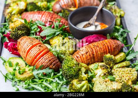 Salade de légumes cuits au four avec vinaigrette tahini sur une poêle en fonte. Patate douce cuite, brocoli et courgettes cuites avec de l'arugula. Concept de nourriture végétalienne saine. Banque D'Images