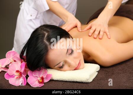 Belle jeune femme dans le salon de spa se massant avec des pierres de spa, sur fond sombre Banque D'Images