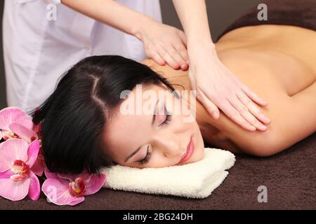 Belle jeune femme dans le salon de spa se massant avec des pierres de spa, sur fond sombre Banque D'Images