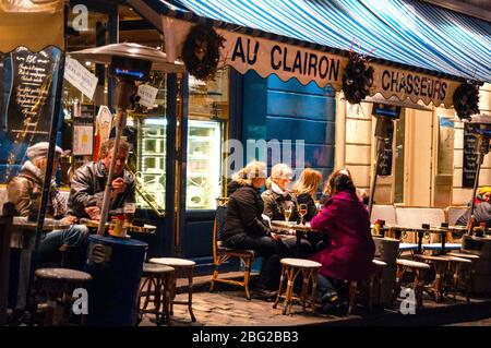 Des amis se rassemblent sous des lampes chauffantes dans le quartier artistique de Montmartre à Paris, en France. Banque D'Images