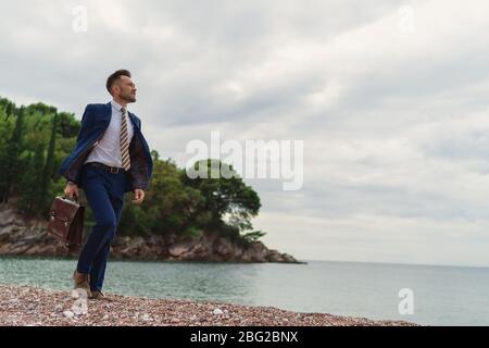 Homme d'affaires marchant sur la plage tenant dans la mallette à main Banque D'Images