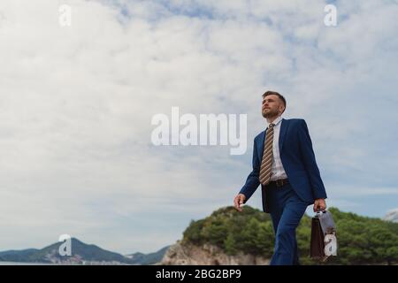 Homme d'affaires marchant sur la plage tenant dans la mallette à main Banque D'Images