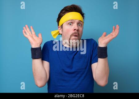 Jeune homme portant un maillot de sport choqué par l'expression surprise et le visage excité. Studio tourné sur un mur bleu. Banque D'Images