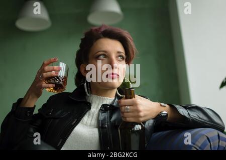 Jeune femme triste avec des cheveux roses foncé avec un look de rock glam est boire du whisky à partir d'un verre avec grimace d'abomination sur le visage, l'alcoolisme féminin Banque D'Images