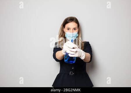 femme d'affaires élégante portant un masque de protection et des gants portant une bouteille de désinfectant dans les mains Banque D'Images