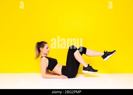 femme athlétique dans la sportwear extestaise son abs, faisant un exercice de sport sur le sol pour les hanches et l'abs, sur fond jaune Banque D'Images