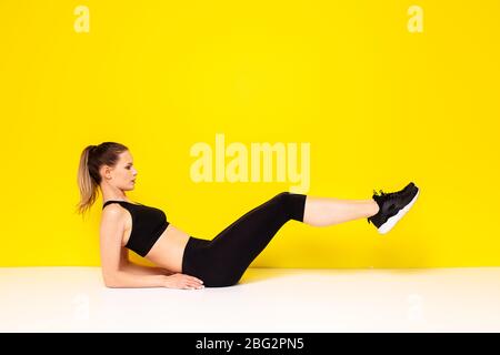 femme athlétique dans la sportwear extestaise son abs, faisant un exercice de sport sur le sol pour les hanches et l'abs, sur fond jaune Banque D'Images