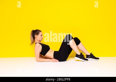 femme athlétique dans la sportwear extestaise son abs, faisant un exercice de sport sur le sol pour les hanches et l'abs, sur fond jaune Banque D'Images