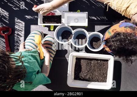 vue de dessus d'une mère et d'une fille dans le balcon de leur maison préparant la saleté dans des pots pour planter des graines, des passe-temps à la maison, durable et écologique Banque D'Images