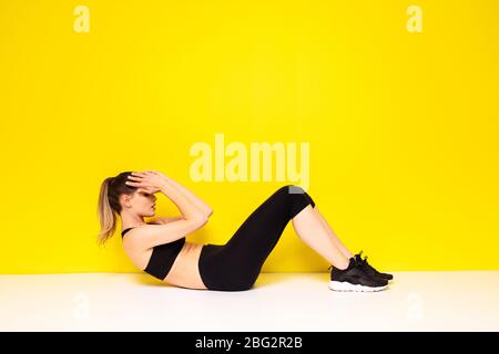 femme athlétique dans la sportwear extestaise son abs, faisant un exercice de sport sur le sol pour les hanches et l'abs, sur fond jaune Banque D'Images