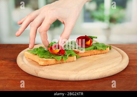 Processus de préparation des petits pains salami sur pain grillé, sur fond lumineux: La main féminine met le rouleau salami avec un morceau de paprika sur pain grillé Banque D'Images