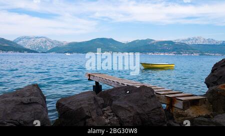 Côte rocheuse avec jetée en bois vers de belles montagnes et la mer avec un bateau jaune sur elle Banque D'Images